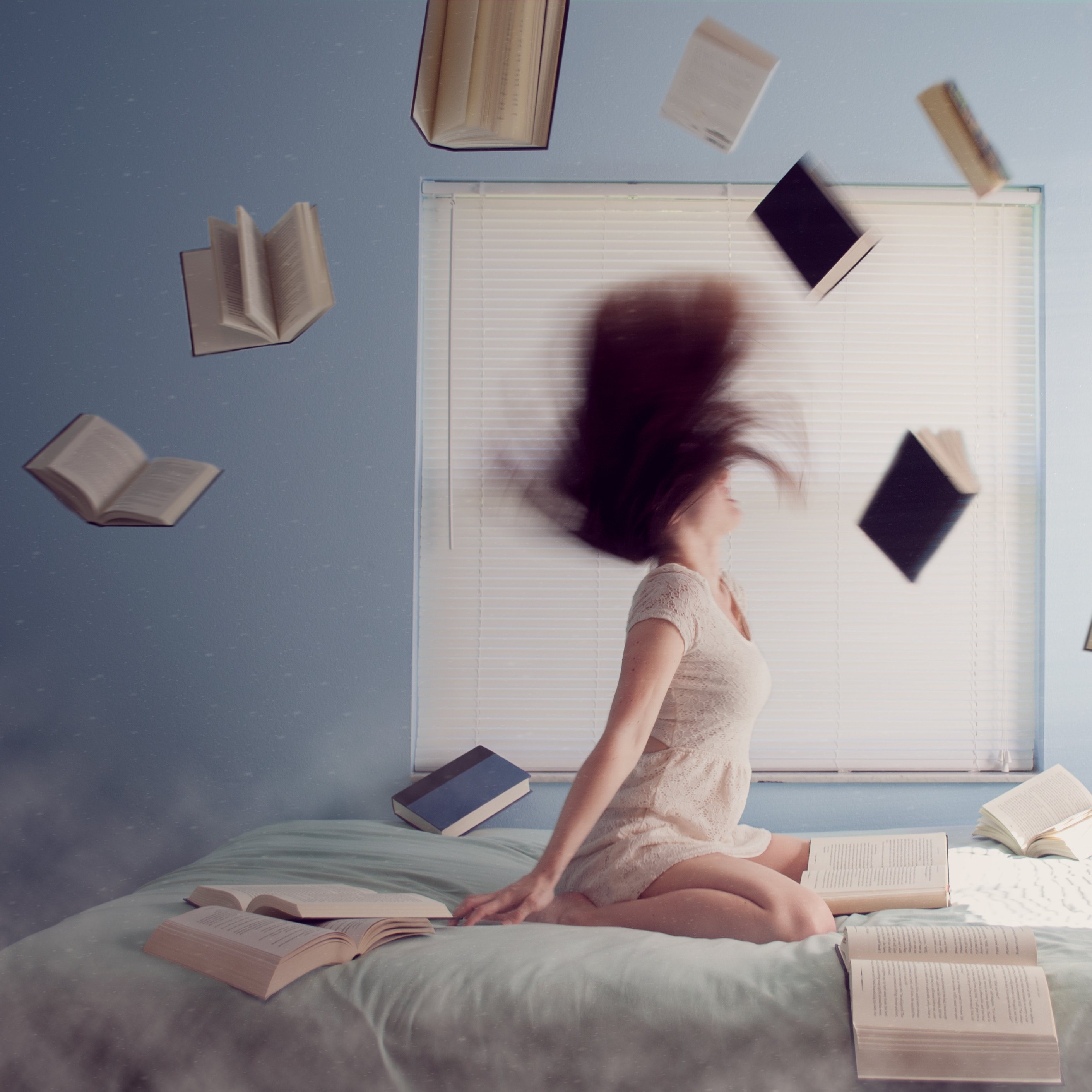 Woman sitting on bed with flying books
